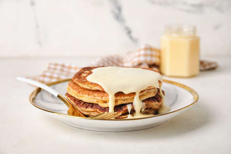 Tasty pancakes with condensed milk on light background
