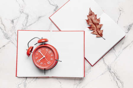 Blank open books, autumn leaf and alarm clock on light background