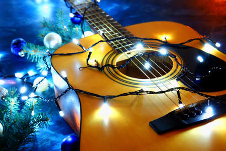 Guitar with Christmas lights and decor on color background