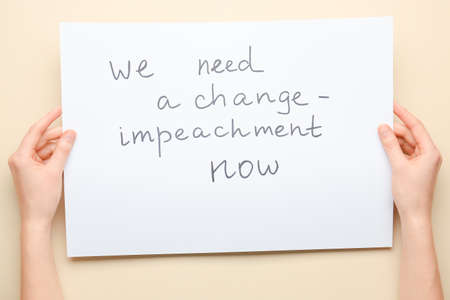 Hands holding paper with text WE NEED A CHANGE - IMPEACHMENT NOW on color background