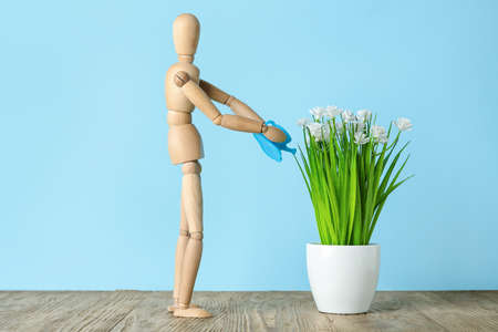 Wooden mannequin watering plant on color background. Concept of gardeningの写真素材