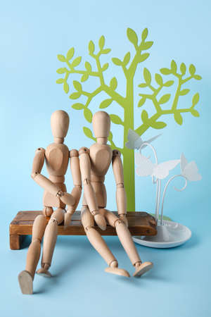 Wooden mannequins sitting on bench on color background