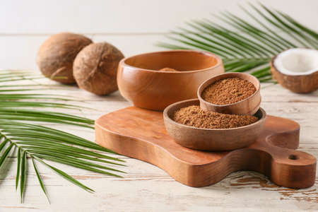 Sweet coconuts and bowls of sugar on light wooden background