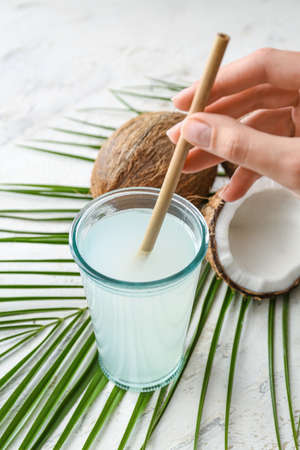 Woman putting straw in glass of fresh coconut water on tableの写真素材
