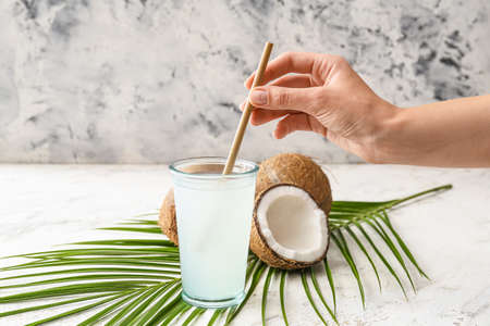 Woman putting straw in glass of fresh coconut water on tableの写真素材