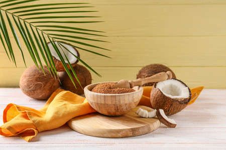 Bowl of sugar and sweet coconuts on light wooden background