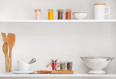 Jars with different spices and kitchen utensils on shelves in kitchenの写真素材