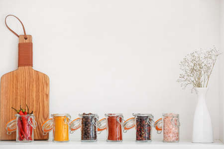 Jars with different spices and wooden board on shelf in kitchenの写真素材