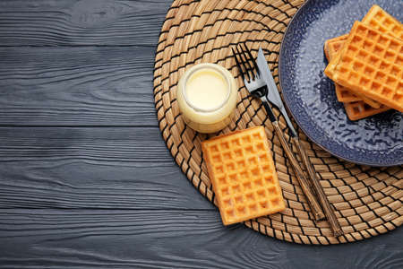 Jar with sweet condensed milk and waffles on dark wooden backgroundの写真素材