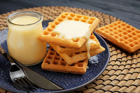 Jar with sweet condensed milk and waffles on tableの写真素材