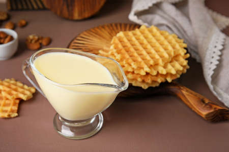 Gravy-boat with sweet condensed milk and waffles on color backgroundの写真素材