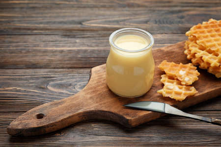 Jar with sweet condensed milk and waffles on wooden backgroundの写真素材