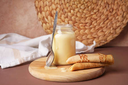 Jar with sweet condensed milk and thin pancakes on color backgroundの写真素材