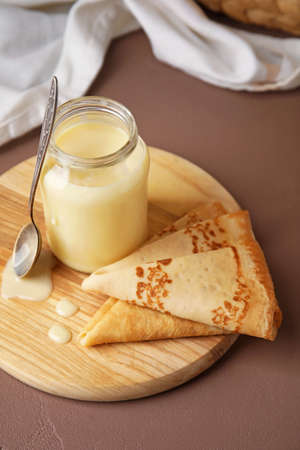 Jar with sweet condensed milk and thin pancakes on color backgroundの写真素材