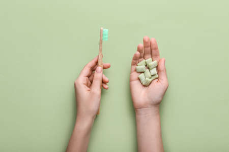 Female hand with chewing gums and toothbrush on color backgroundの写真素材