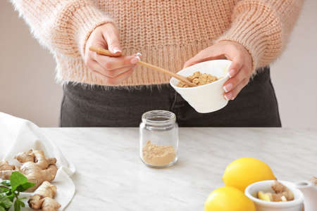 Woman putting ginger powder into jar on table in kitchenの写真素材