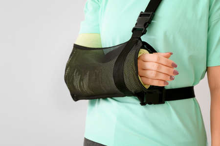 Young woman with broken arm on light backgroundの写真素材