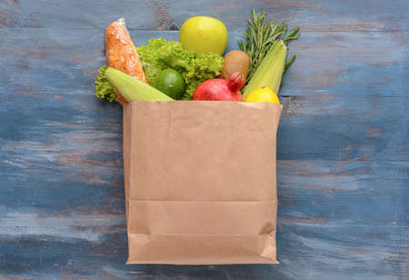 Paper bag with different products on color wooden background