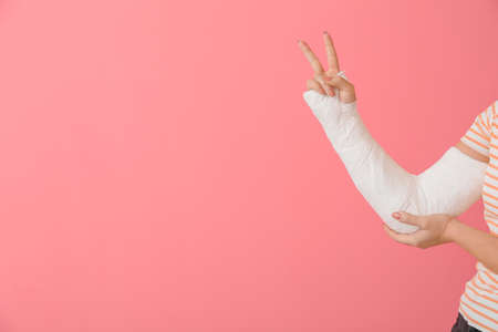 Young woman with broken arm showing victory gesture on color backgroundの写真素材