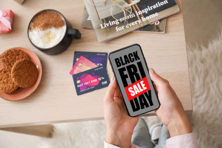 Young woman with mobile phone shopping online on Black Friday at homeの写真素材