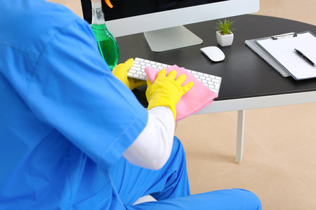 Male janitor cleaning computer in officeの写真素材