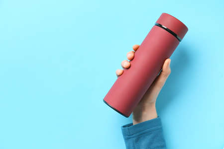 Female hand with modern thermos on color backgroundの写真素材
