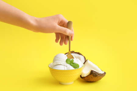 Female hand and bowl with tasty coconut ice cream on color background