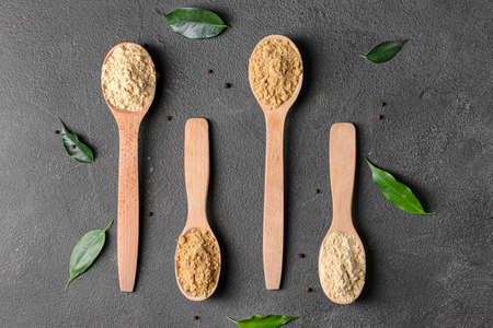 Spoons with ginger powder and green leaves on dark backgroundの写真素材