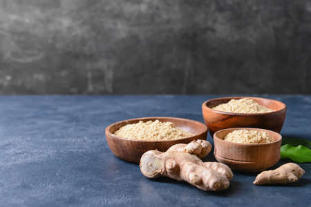 Bowls with ginger powder and roots on color backgroundの写真素材
