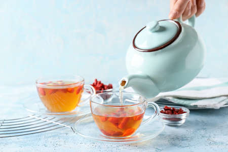 Woman pouring tasty tea with goji berries from teapot into glass cup on tableの写真素材
