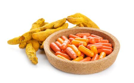 Bowl with turmeric pills and roots on white backgroundの写真素材