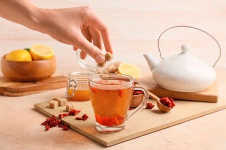 Female hand and hot tea with goji berries on color backgroundの写真素材