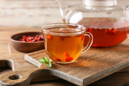 Teapot and glass cup of hot tea with goji berries on wooden backgroundの写真素材