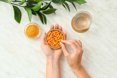 Female hands with turmeric pills on light backgroundの写真素材