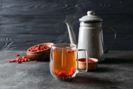 Teapot and glass cup of hot tea with goji berries on dark backgroundの写真素材