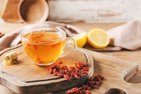 Glass cup of hot tea with goji berries on light wooden backgroundの写真素材