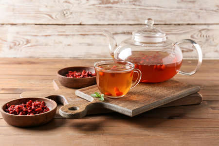 Teapot and glass cup of hot tea with goji berries on wooden backgroundの写真素材