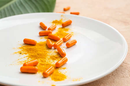 Plate with turmeric pills and powder on color backgroundの写真素材