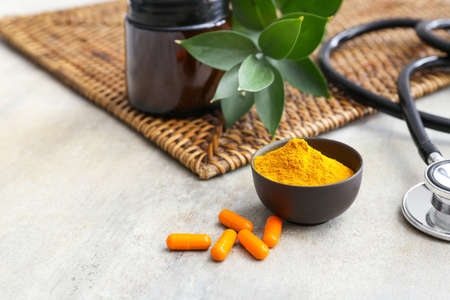 Turmeric pills, bowl with powder and stethoscope on light backgroundの写真素材
