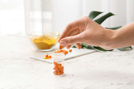 Female hand and bottle with turmeric pills on light backgroundの写真素材