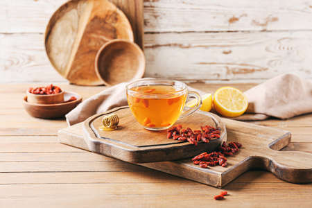 Glass cup of hot tea with goji berries on light wooden backgroundの写真素材