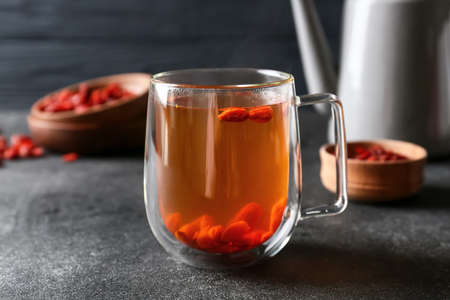 Teapot and glass cup of hot tea with goji berries on dark backgroundの写真素材