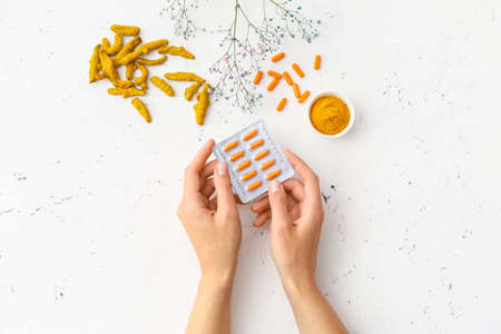 Female hands and blister pack with turmeric pills on light backgroundの写真素材