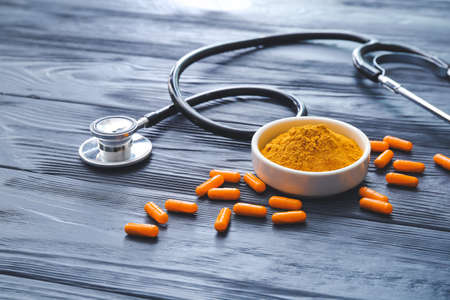 Turmeric pills, powder and stethoscope on dark wooden background