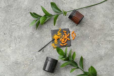 Turmeric pills and spoon with powder on gray background