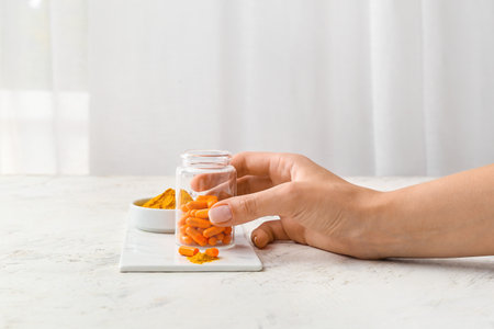 Female hand with bottle of turmeric powder pills on light backgroundの写真素材