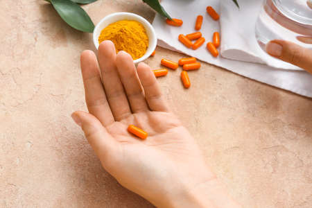 Female hand with turmeric pill and powder on color backgroundの写真素材
