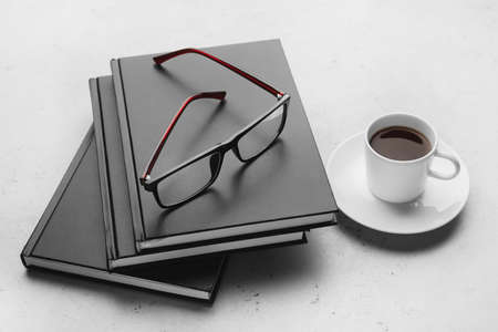 Stack of books, eyeglasses and cup of coffee on light backgroundの写真素材