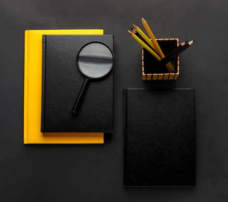 Different books, pencils and magnifier on dark backgroundの写真素材