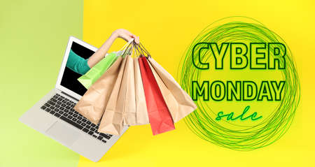 Woman sticking hand with shopping bags out of laptop screen on color background. Cyber Monday Saleの写真素材